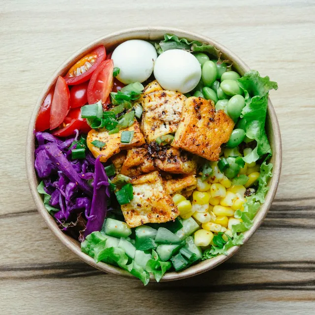 A salad bowl with boiled eggs, grilled tofu, corn, cucumber and red cabbage